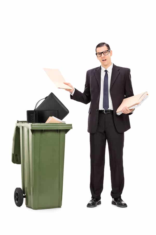 A business person throwing files into a large trash bin.