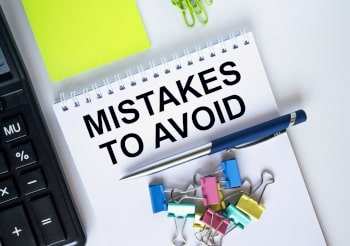 A notepad with the words Mistakes to Avoid on a desk with other supplies.